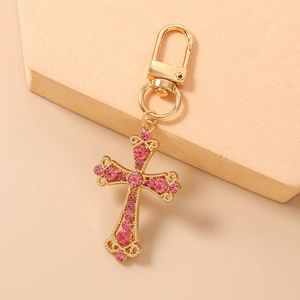Vue détaillée du porte-clés croix dorée avec strass roses sur un fond de ton chaud