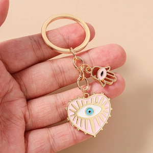 Porte-clés cœur rose avec œil et main de Fatma, tenu à la main sur fond beige clair