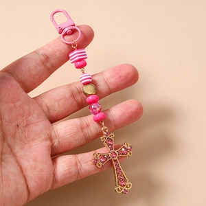 Détail de perles en résine rayées roses et d'une croix en strass sur un porte-clés doré chic