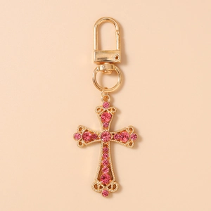 Détail d'un porte-clés croix dorée orné de strass roses et d'un fermoir en forme de D