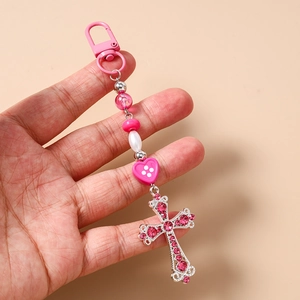 Gros plan d'un porte-clés perlé rose avec un pendentif croix en argent serti de strass