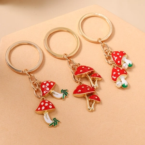 Three red mushroom keychains with faux pearls and green leaves on gold alloy rings