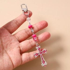 Détail d'un porte-clés croix en perles roses tenu à la main avec strass et mousqueton métal
