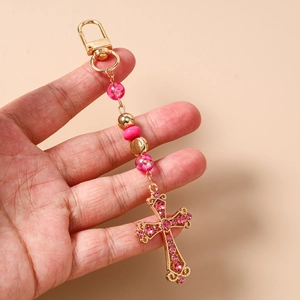 Détail du porte-clés croix en strass rose avec perles rayées et fermoir doré