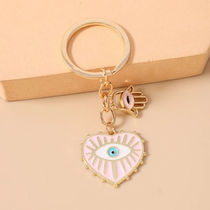 Détail du porte-clés œil maléfique en cœur rose avec breloque main de Hamsa dorée
