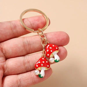 Detail of hand holding a golden keychain with red mushroom charms and white pearls