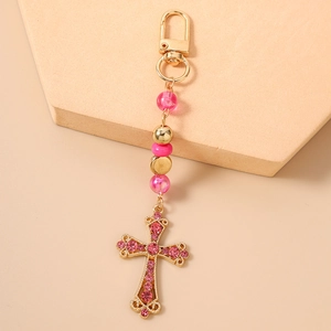 Gros plan détaillé d'un porte-clés croix dorée avec strass roses et perles élégantes