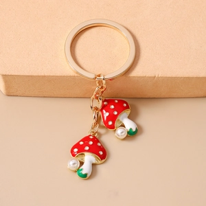 Detail of mushroom charms on gold keychain with red enamel patterns and small white pearls