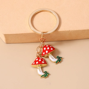 Detailed view of red polka dot mushroom keychain with gold ring and green leaf accents
