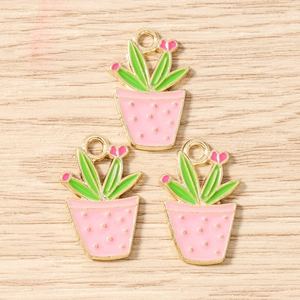 Detailed view of three pink cactus enamel charms with golden edges on wood texture