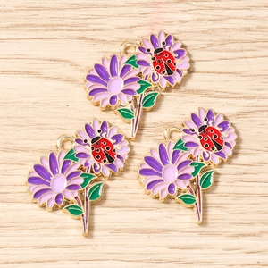 Dettaglio di tre ciondoli a margherita viola con coccinelle e finiture in metallo oro