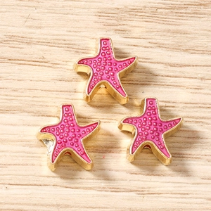 Dettaglio di tre ciondoli a forma di stella marina in smalto rosa con bordo dorato