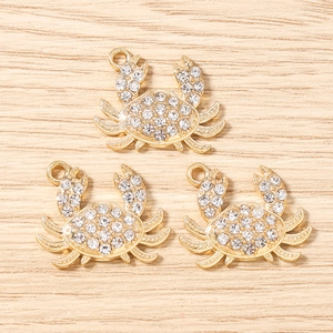 Détail macro de trois breloques crabe dorées serties de strass sur fond en bois