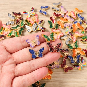 Detail of colorful enamel butterfly pendants being held to show small size for jewelry DIY