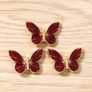 Detailed view of three wine red enamel butterfly pendants with golden metal edges