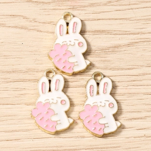 Detailed macro view of three white and pink enamel cartoon rabbit charms with golden edges
