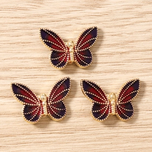Detail view of purple and red enamel butterfly jewelry charms on a light wood surface