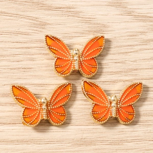 Detailed macro view of three orange enamel butterfly pendants on wood background