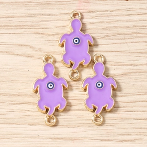 Close-up of turtle pendants with purple enamel and evil eye symbol on wood background