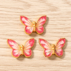 Macro detail of pink enamel butterfly pendants with golden beaded edges on wood