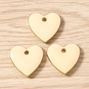 Detailed close-up of cream enamel heart charms with gold edges for DIY jewelry making