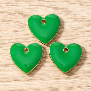 Macro detail of three green heart enamel charms with gold plating for DIY jewelry