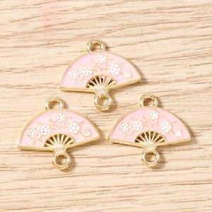 Detailed macro view of pink enamel fan-shaped charms with white plum blossom patterns for DIY