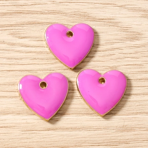 Detail view of pink enamel heart pendants with gold metal edges on a light wood background