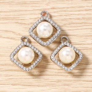 Macro view of three square rhinestone geometric pendants with white pearls on wood surface
