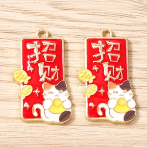 Détail macro de breloques chat porte-bonheur en émail rouge avec calligraphie dorée pour bijoux