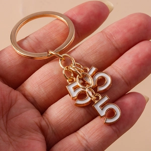 Detail of hand-held gold keychain with white enamel charms showing numbers five and three