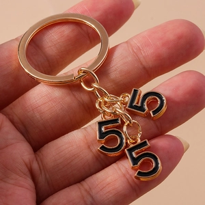 Close-up of a gold keychain with three black enamel number 5 charms on a hand