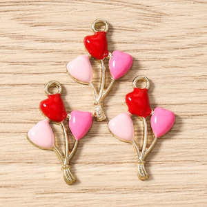 Close-up of heart-shaped balloon charms in red and pink enamel on a wooden surface