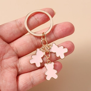 Detalle de colgantes de oso rosa y anillo de aleación dorado sostenidos a mano sobre beige