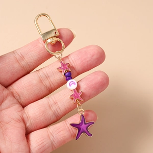 Detail of purple starfish beaded keychain with gold hook and moon charm on hand