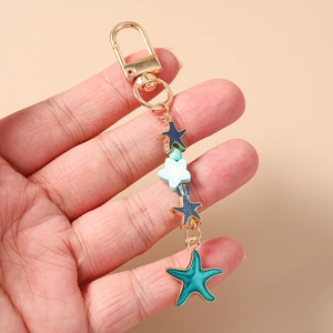 Detail of colorful starfish charms in blue and white held by hand with gold lobster clasp