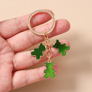 Detalle de tres dijes de oso de esmalte verde en un llavero de metal dorado sostenido a mano