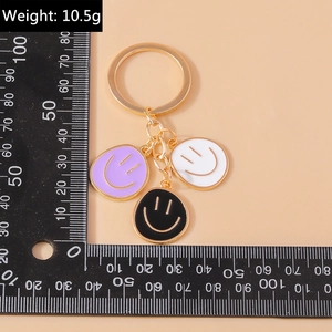 Three-color smiley face keychains in purple, black, and white with golden metal finish