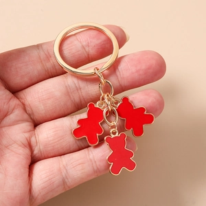 Detalle de tres dijes de oso de esmalte rojo en un llavero de metal dorado sostenido a mano
