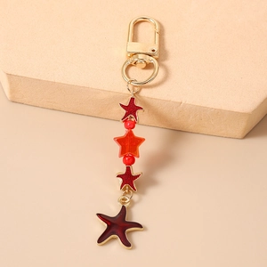 Detail of red and orange enamel starfish keychain with golden metal hook on beige display
