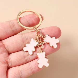 Detalle de colgantes de ositos rosas en un llavero dorado sostenido sobre fondo beige