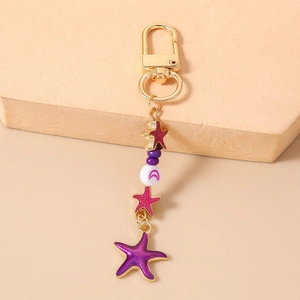 Detail of star-shaped enamel pendants on a gold lobster clasp keychain in pink background