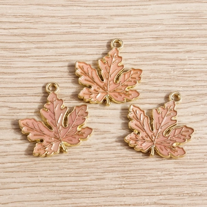 Detail von Ahornblatt-Anhängern aus Emaille in Pink und Gold auf hellem Holzgrund