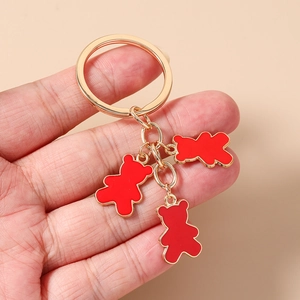 Detalle de un llavero dorado con tres dijes de osos en esmalte rojo y metalizado