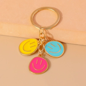 Detail of colorful smiley face pendants on a polished gold keyring with three enamel charms