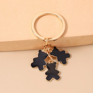 Detalle de llavero dorado con tres colgantes de oso en esmalte negro sobre bloque beige