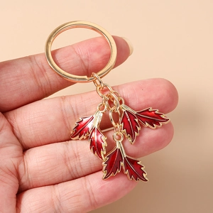 Detail of red enamel maple leaf charms on a golden keychain held by a hand