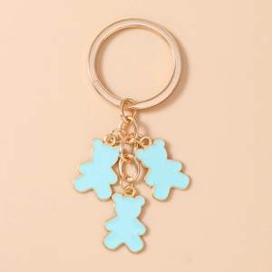 Detalle de un llavero dorado con tres colgantes de osos en esmalte azul claro para bolsos