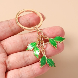 Detail of hand-held gold keychain with three green enamel leaf pendants and links