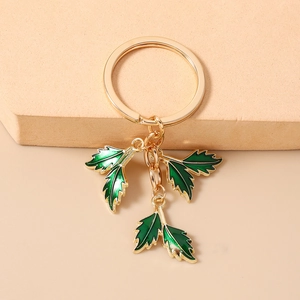 Detail of golden metal keychain with three green enamel leaf pendants on a beige stand